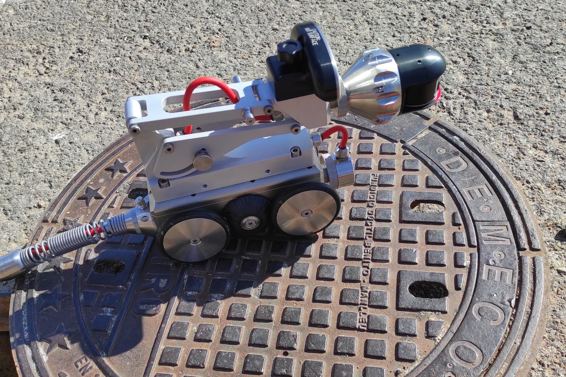 Robot de videoinspección apoyado sobre una tapa de alcantarillado abierta.